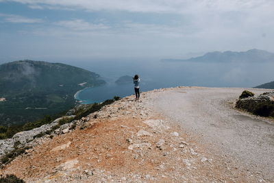 Rear view of woman standing at mountain peak against sky