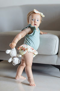 Full length of cute baby girl sitting on sofa at home