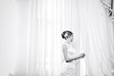 Bride standing by window curtain