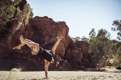 Man dancing on sand against rock formations at desert during sunny day