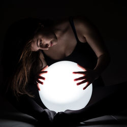 Young woman looking at glowing lamp in darkroom