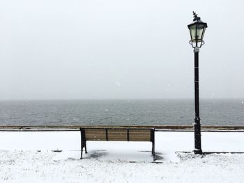 Bench on street by sea against sky during winter