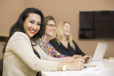 Portrait of happy businesswoman with colleagues sitting at conference table in creative office