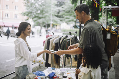 Father doing online payment to vendor during shopping with kids at flea market