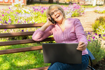 Woman holding mobile phone while sitting outdoors