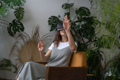 Young woman wearing vr helmet touching air with finger, testing modern hi-tech future gadget at home