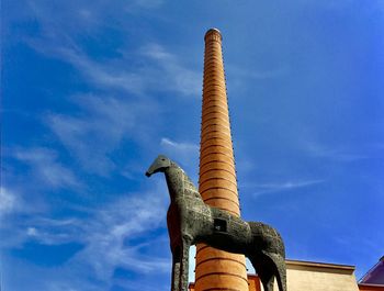 Low angle view of statue of modena and tower against blue sky.