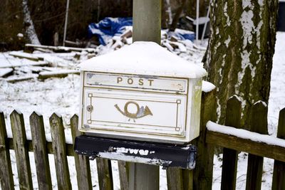 Snow on old post box with text on fence during winter