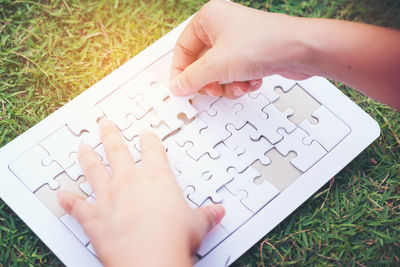 Cropped hands of woman playing jigsaw on grassy field