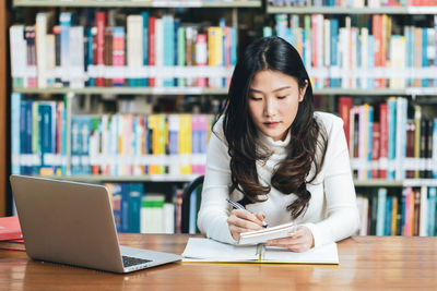 Young woman using phone while sitting on table