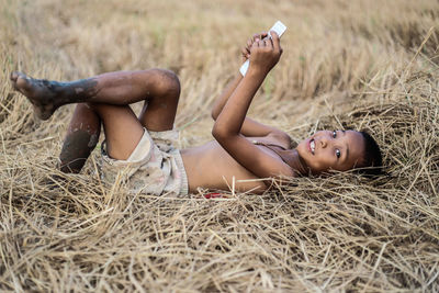 Portrait of boy using mobile phone while lying on field at farm