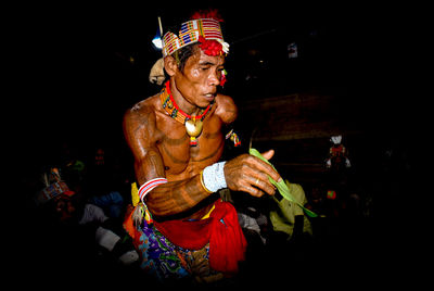 Shirtless man wearing headdress while standing in darkroom