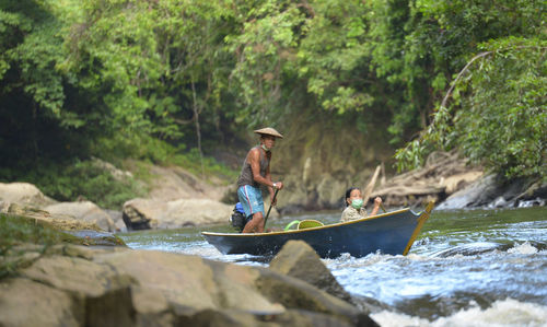 Man on rock by river against trees