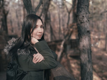 Portrait of woman standing by tree trunk