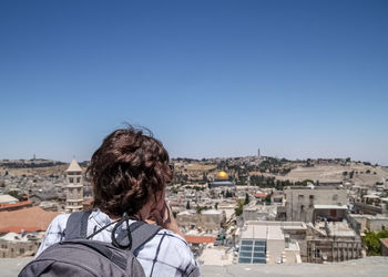 Rear view of woman with backpack looking at cityscape against clear sky