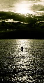 Silhouette person in sea against sky during sunset
