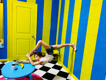 Young girl in unusual pose standing against wall in the living room with a a cup in her hand