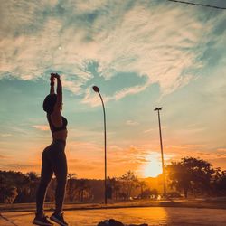 Rear view of silhouette woman standing by street against sky during sunset