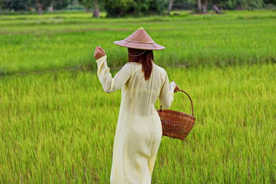 Rear view of vietnamese woman carrying basket while walking at farm