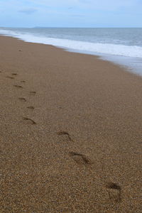 Footprints on sand at beach against sky