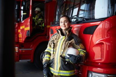 Portrait of confident female firefighter standing by fire truck in fire station