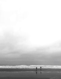 Silhouette people at beach against cloudy sky