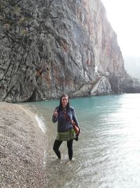 Portrait of woman standing on shore at beach against rock formations