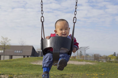 Portrait of cute baby boy sitting on swing against cloudy sky