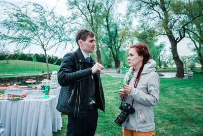 Side view of young couple standing against trees