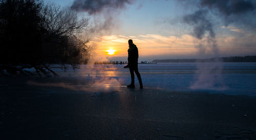 Silhouette man standing on shore against sky during sunset