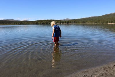 Boy standing in lake against blue sky