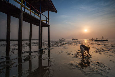 Woman standing on beach by sea against sky during sunset