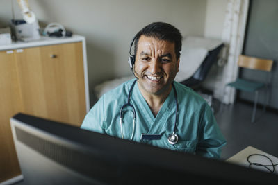 Smiling male doctor wearing headset giving advice through video call in hospital