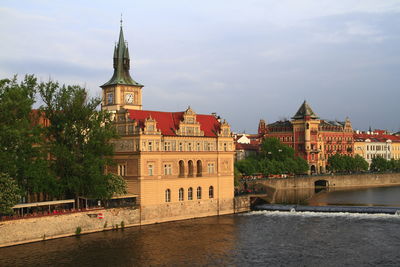View of buildings by river against sky in city