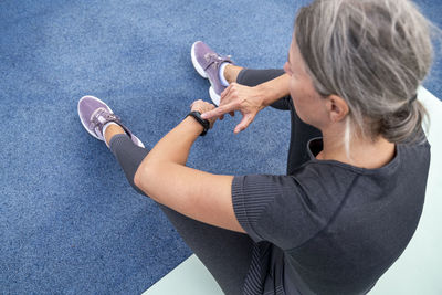 Mature woman checking time in smart watch sitting on exercise mat