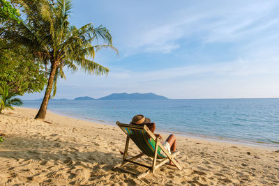 Rear view of woman sitting on beach against sky