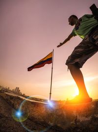 Man standing by flag against sky during sunset