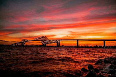 Bridge over calm sea against orange sky