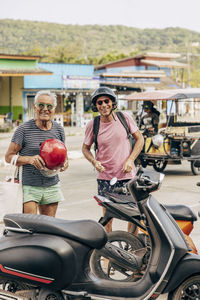 Portrait of happy elderly couple standing near motorcycle on road