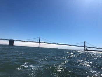 Suspension bridge over sea against clear sky
