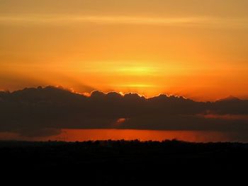 Scenic view of dramatic sky over silhouette landscape during sunset