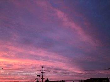 Low angle view of silhouette electricity pylon against dramatic sky