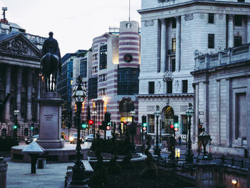 Statue by street against buildings in city at dusk