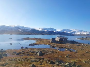Scenic view of lake by snowcapped mountains against clear blue sky