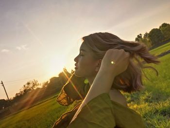 Portrait of young woman looking away on field against sky during sunset