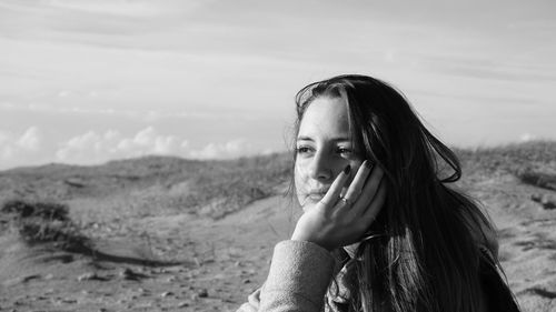 Thoughtful beautiful woman with hand on chin sitting against sky