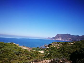 Scenic view of sea by mountain against clear blue sky