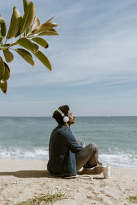 Man with eyes closed listening music through headphones while sitting at beach