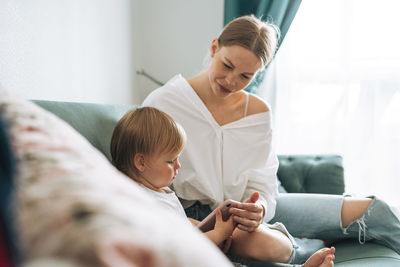 Young mother and cute baby girl using mobile phone at home