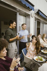 Smiling male friends enjoying drinks with group of friends at dinner party in balcony